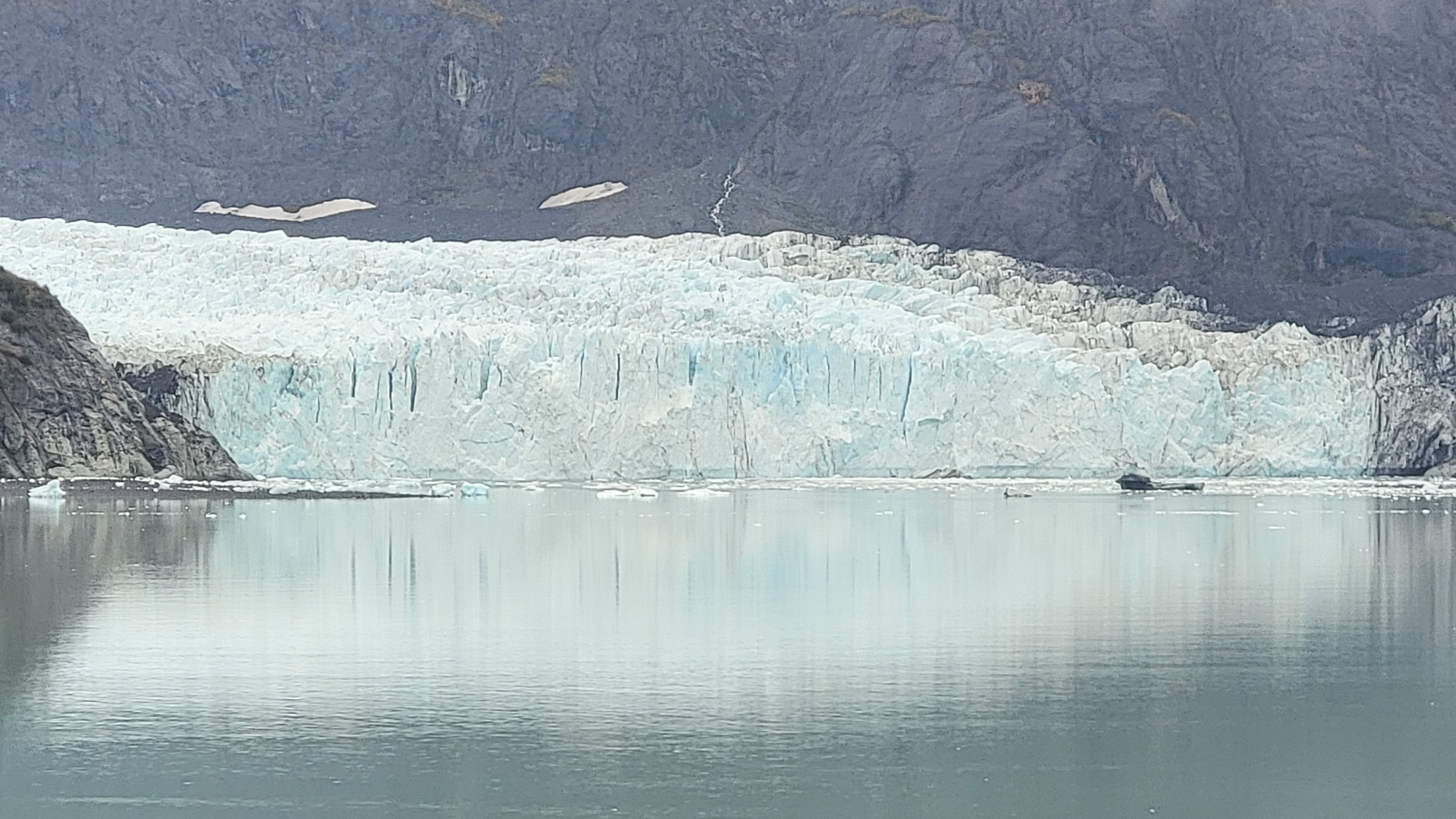 Blue-white glacier face reflected in calm water in Glacier Bay, Alaska.