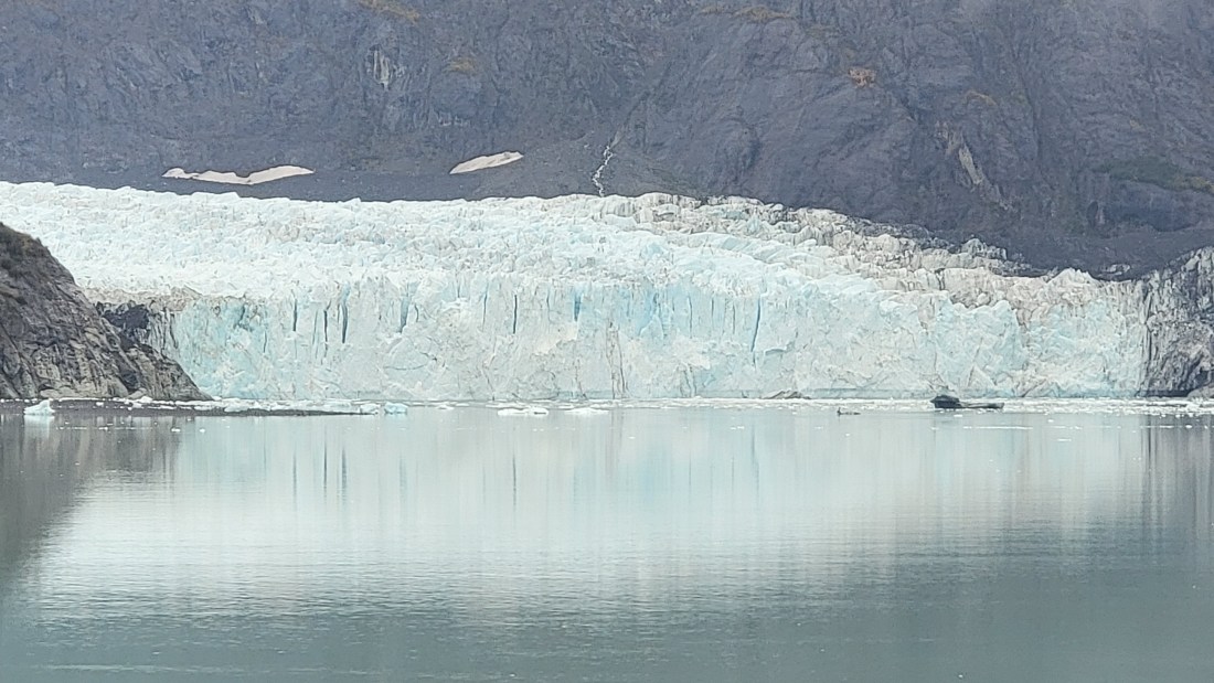 Blue-white glacier face reflected in calm water in Glacier Bay, Alaska.