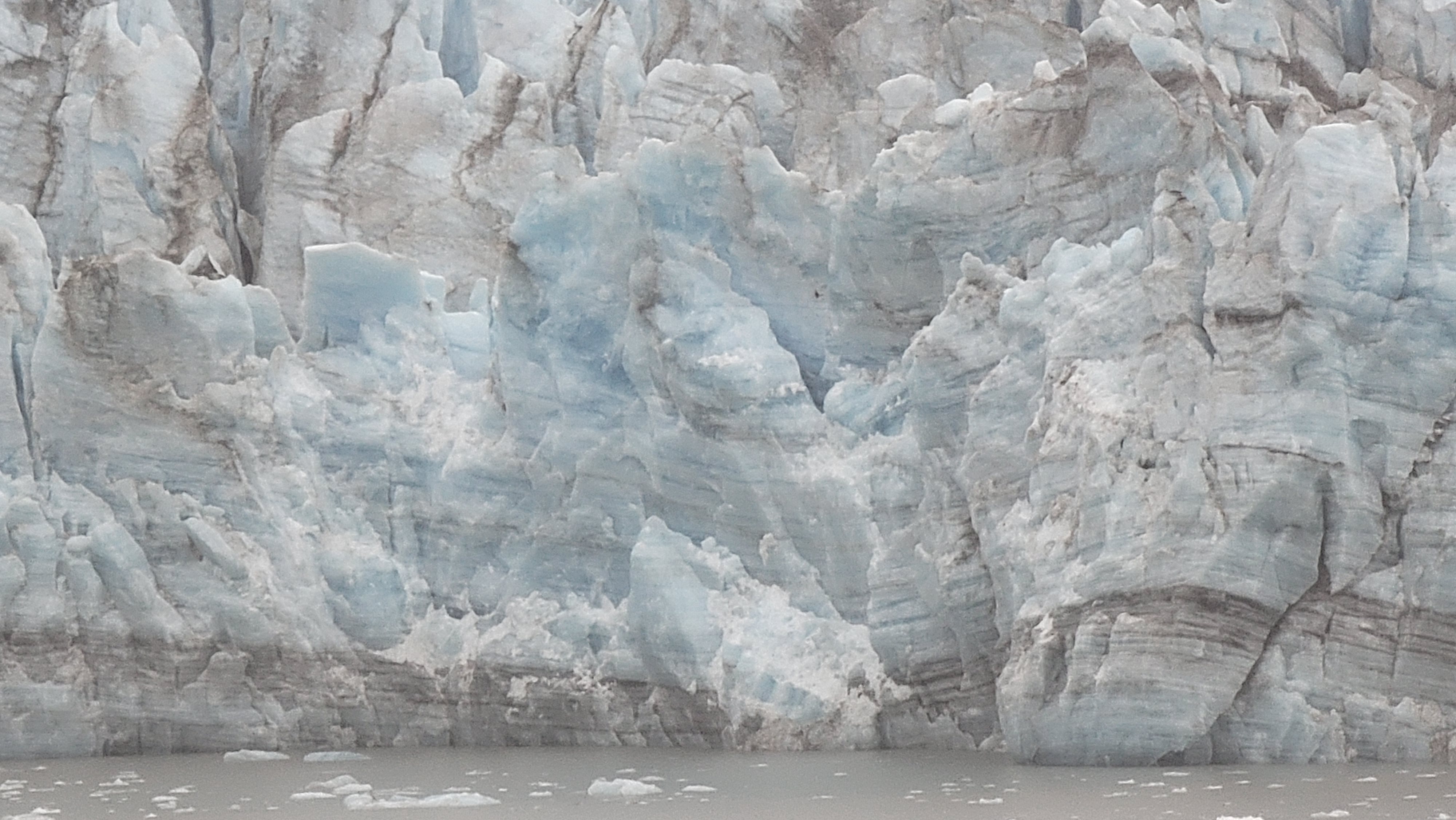 Jagged blue-white glacier ice with dark sediment bands above the water.