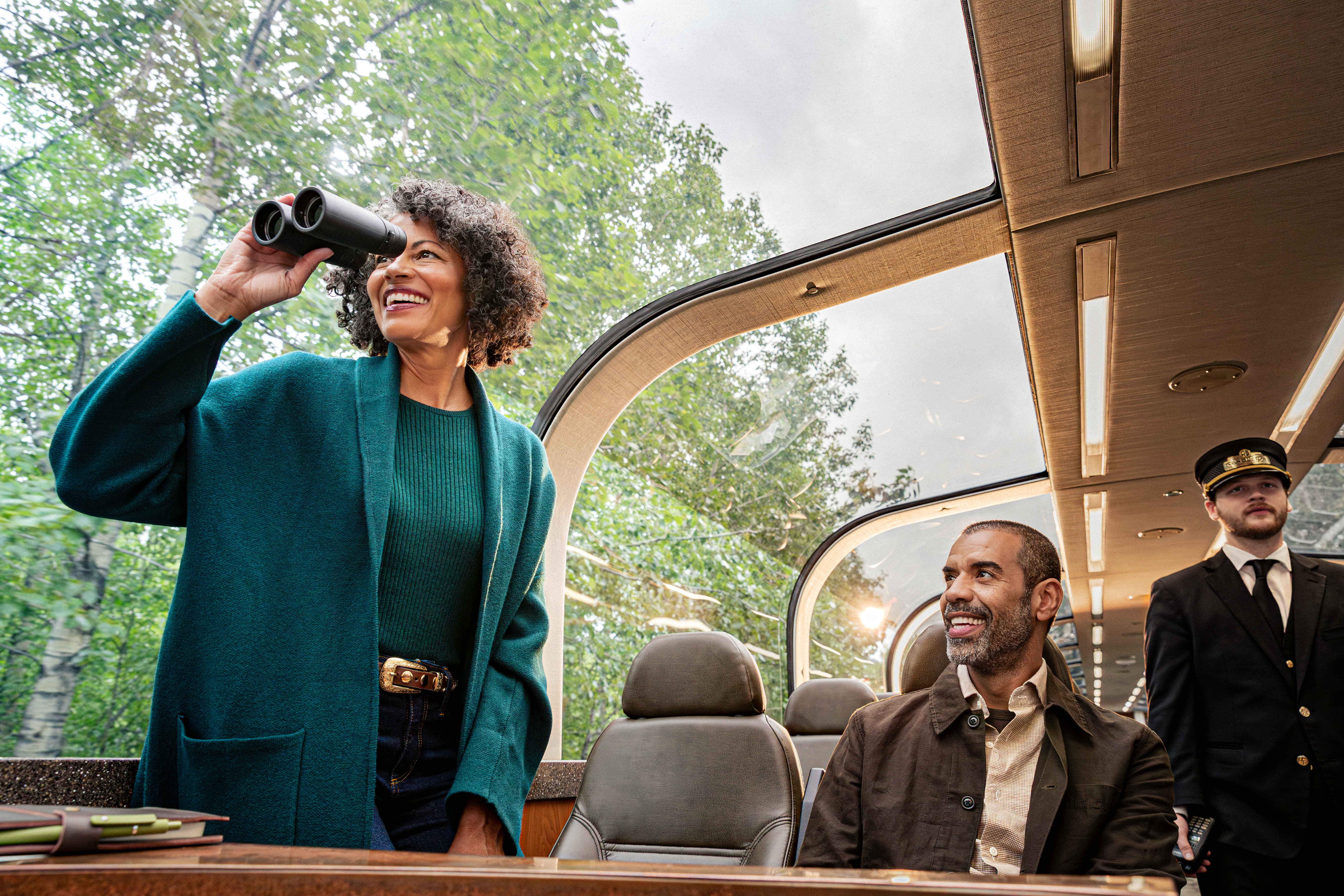Guests looking through the curved windows of a glass-domed railcar, with a conductor nearby.